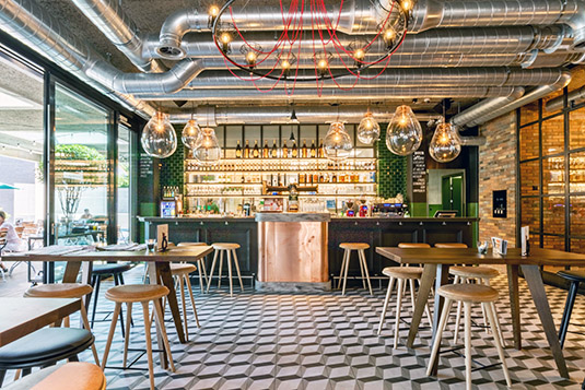 A modern-style cafe with stools and chairs plus a bar at the back of the room