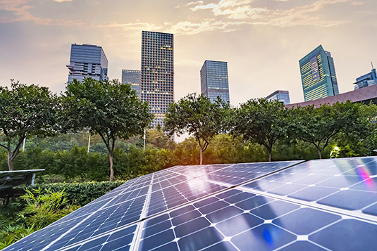 Solar panels on a building with a row of trees and skyscrapers in the background