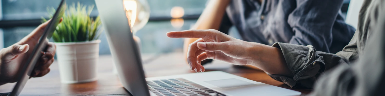 A man's hand pointing at an open laptop on a desk