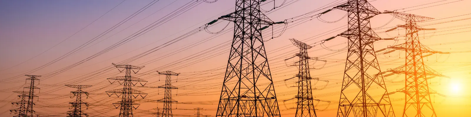 A row of electricity pylons in front of a sunset fading from purple on the left to orange on the right